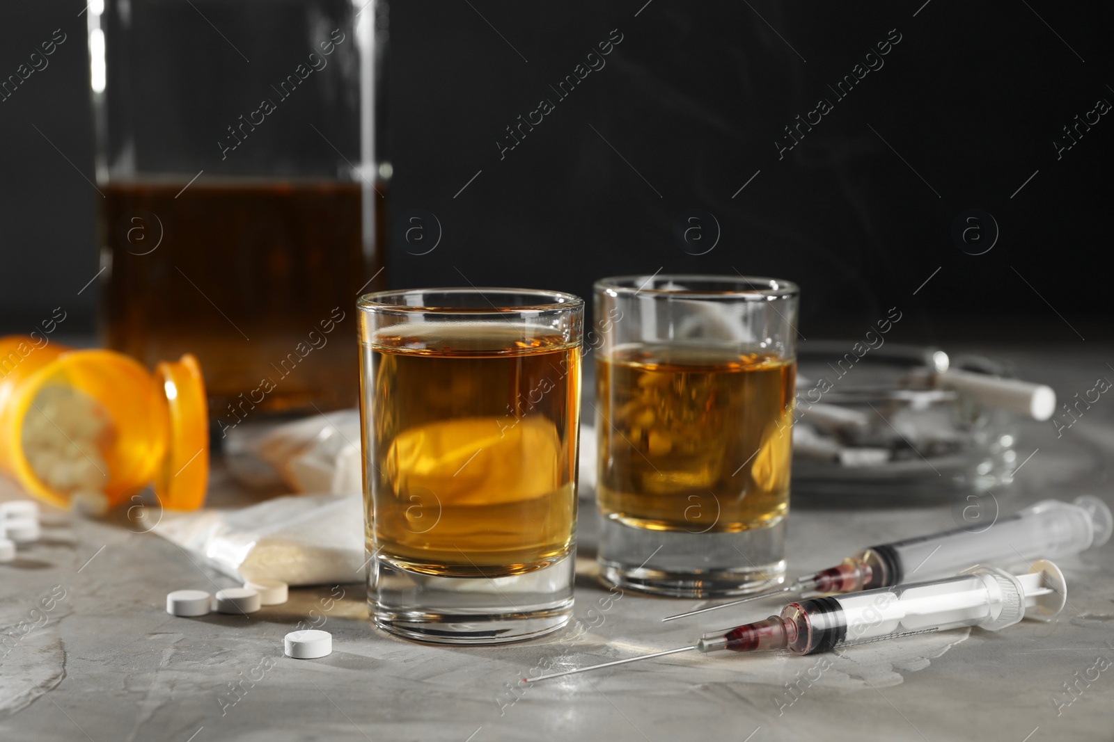 Photo of Alcohol and drug addiction. Whiskey in glasses, syringes, pills and cocaine on grey table