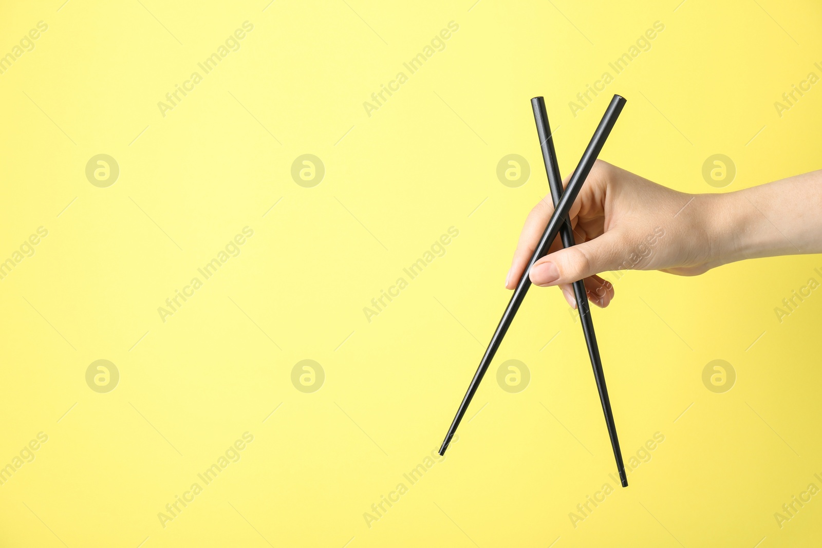 Photo of Woman holding pair of black chopsticks on yellow background, closeup. Space for text