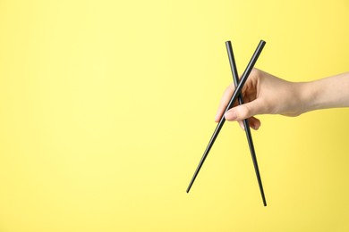 Photo of Woman holding pair of black chopsticks on yellow background, closeup. Space for text