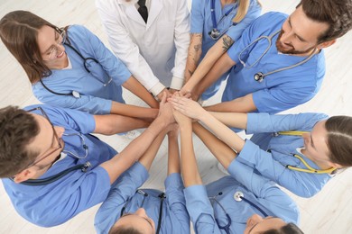 Photo of Doctor and interns stacking hands together indoors, top view