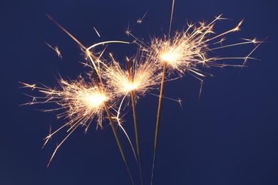 Photo of Bright burning sparkler on blue background, closeup