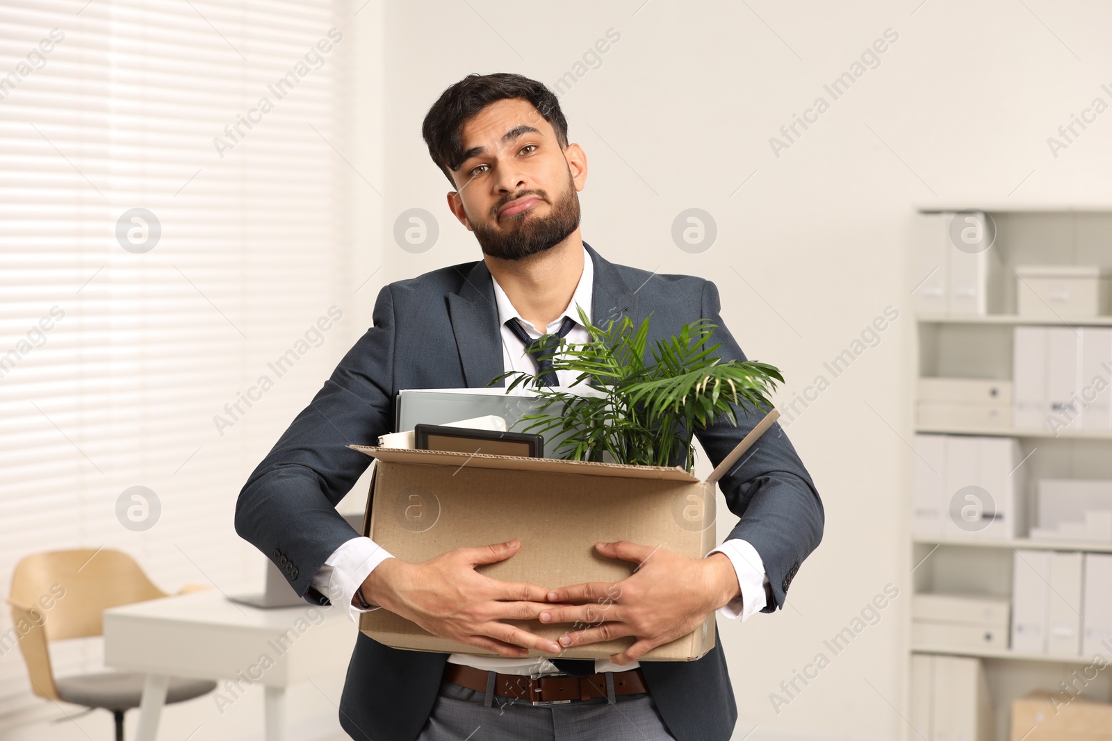 Photo of Unemployment problem. Frustrated man with box of personal belongings in office