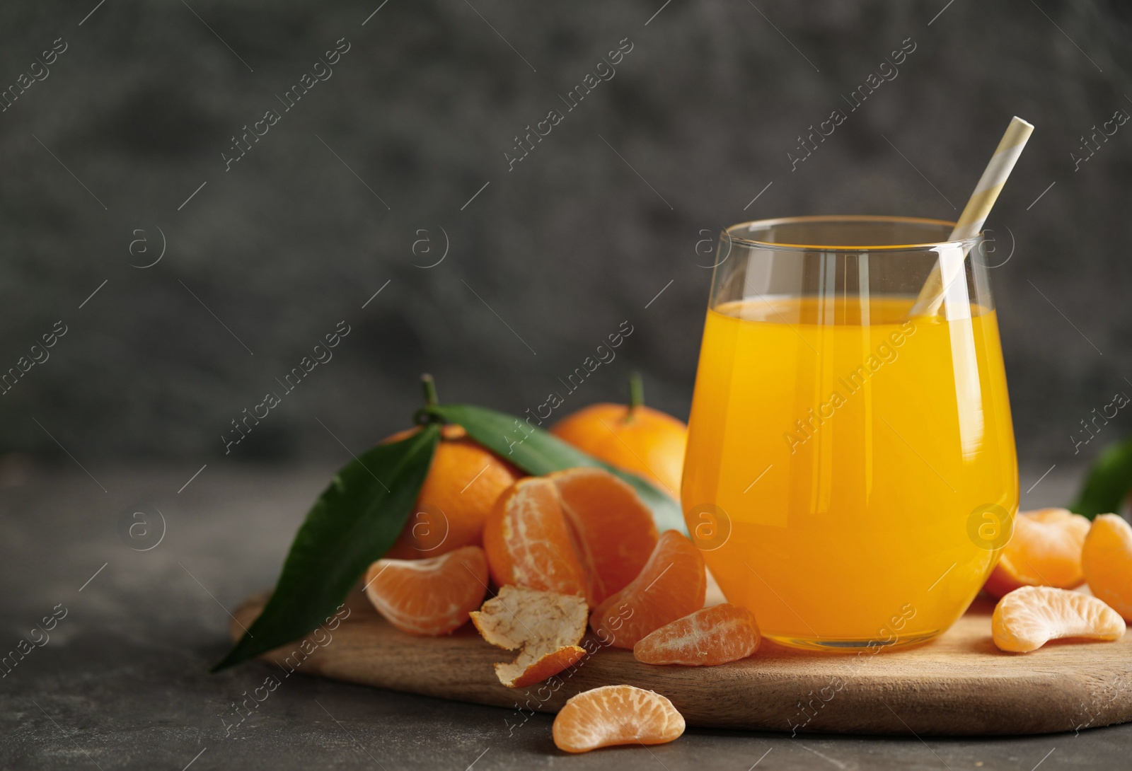 Photo of Fresh tangerines and glass of juice on grey table. Space for text