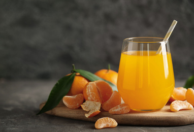 Fresh tangerines and glass of juice on grey table. Space for text