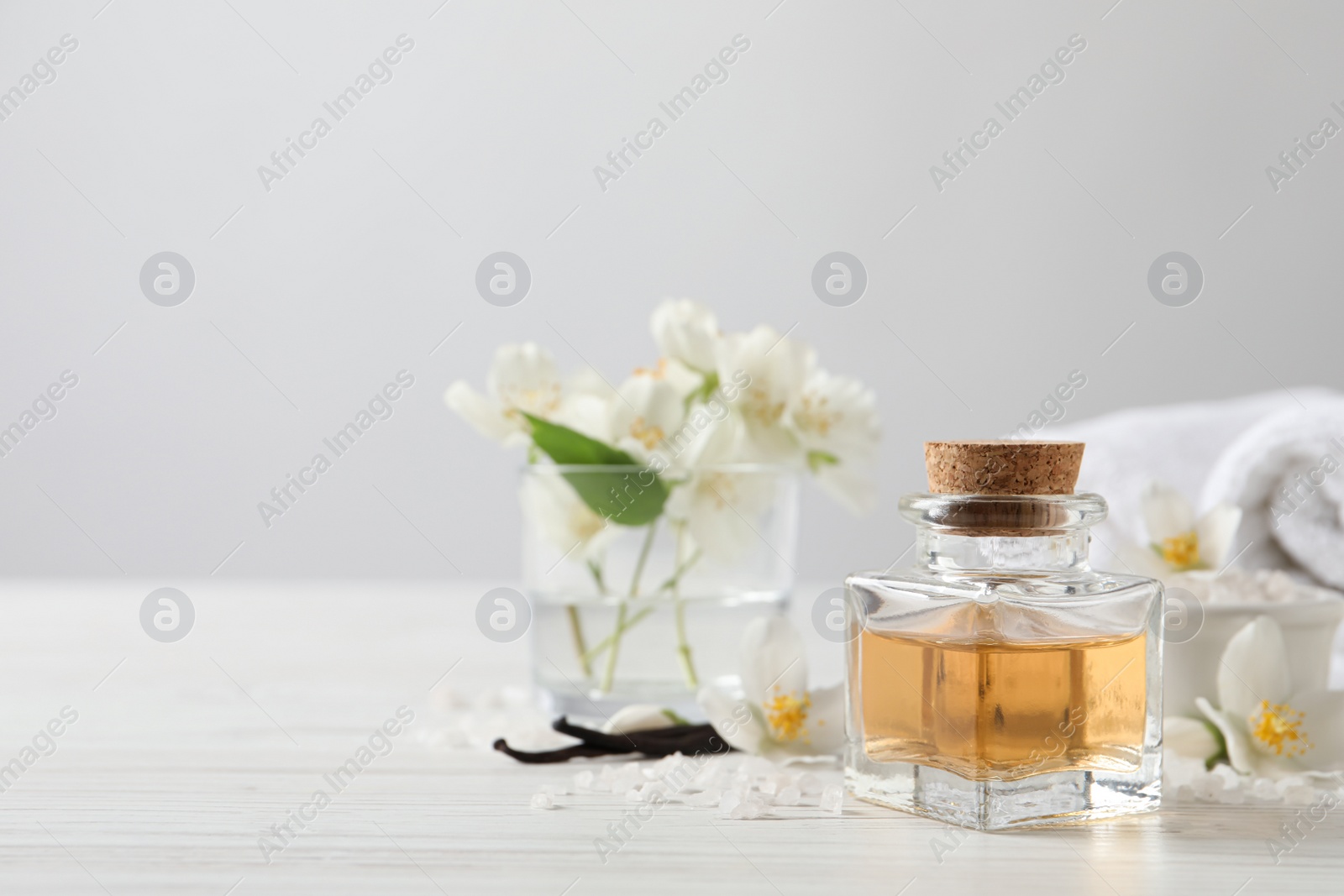 Photo of Beautiful composition with jasmine essential oil and fresh flowers on white wooden table. Space for text