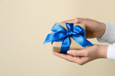 Photo of Woman holding gift box with blue bow on beige background, closeup. Space for text