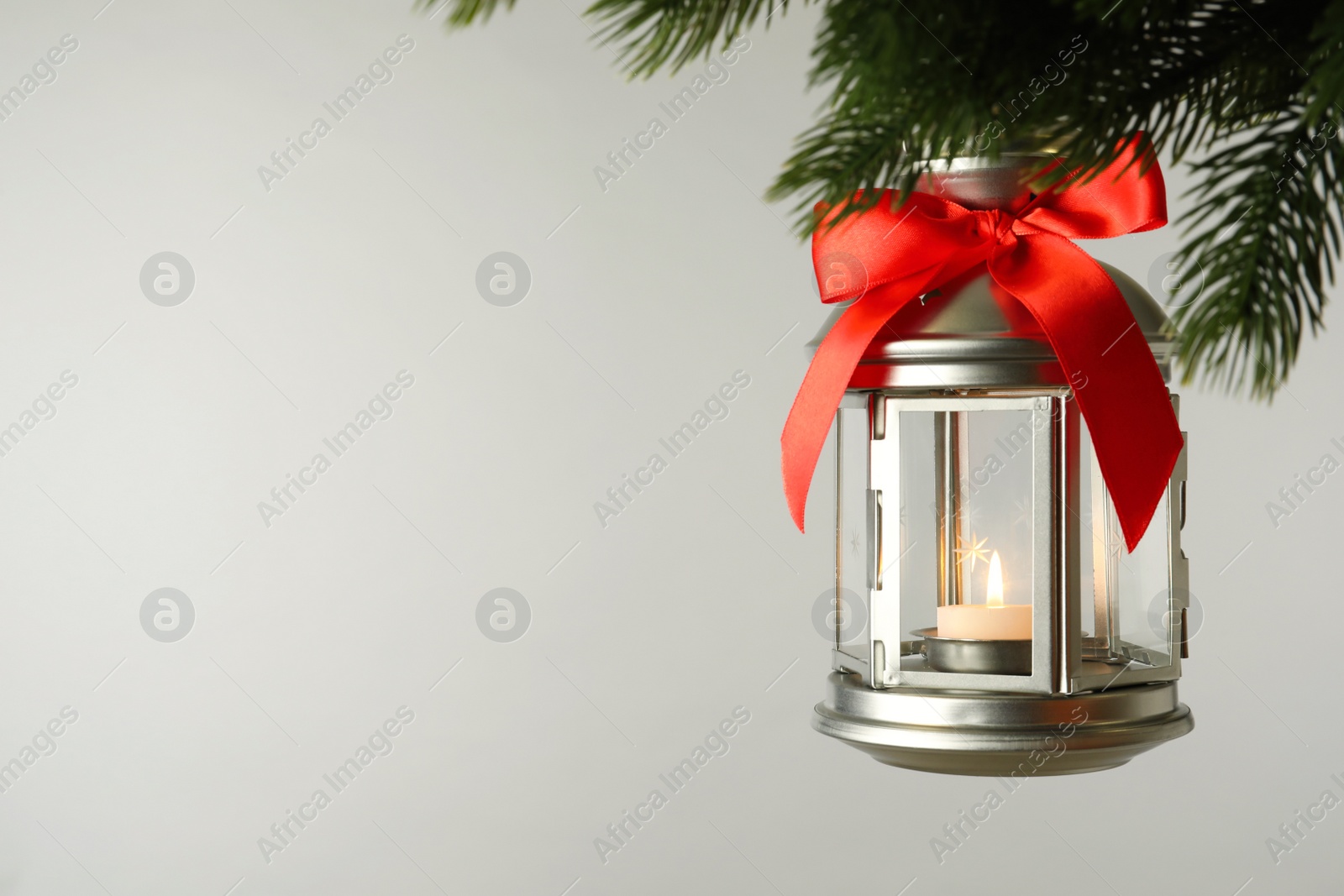 Photo of Christmas lantern with candle hanging on fir tree branch against light background. Space for text