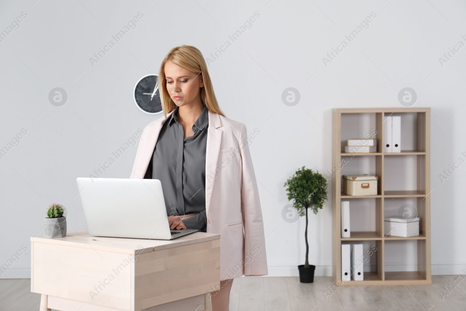 Photo of Young woman using laptop at stand up workplace indoors