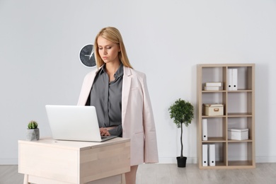 Young woman using laptop at stand up workplace indoors