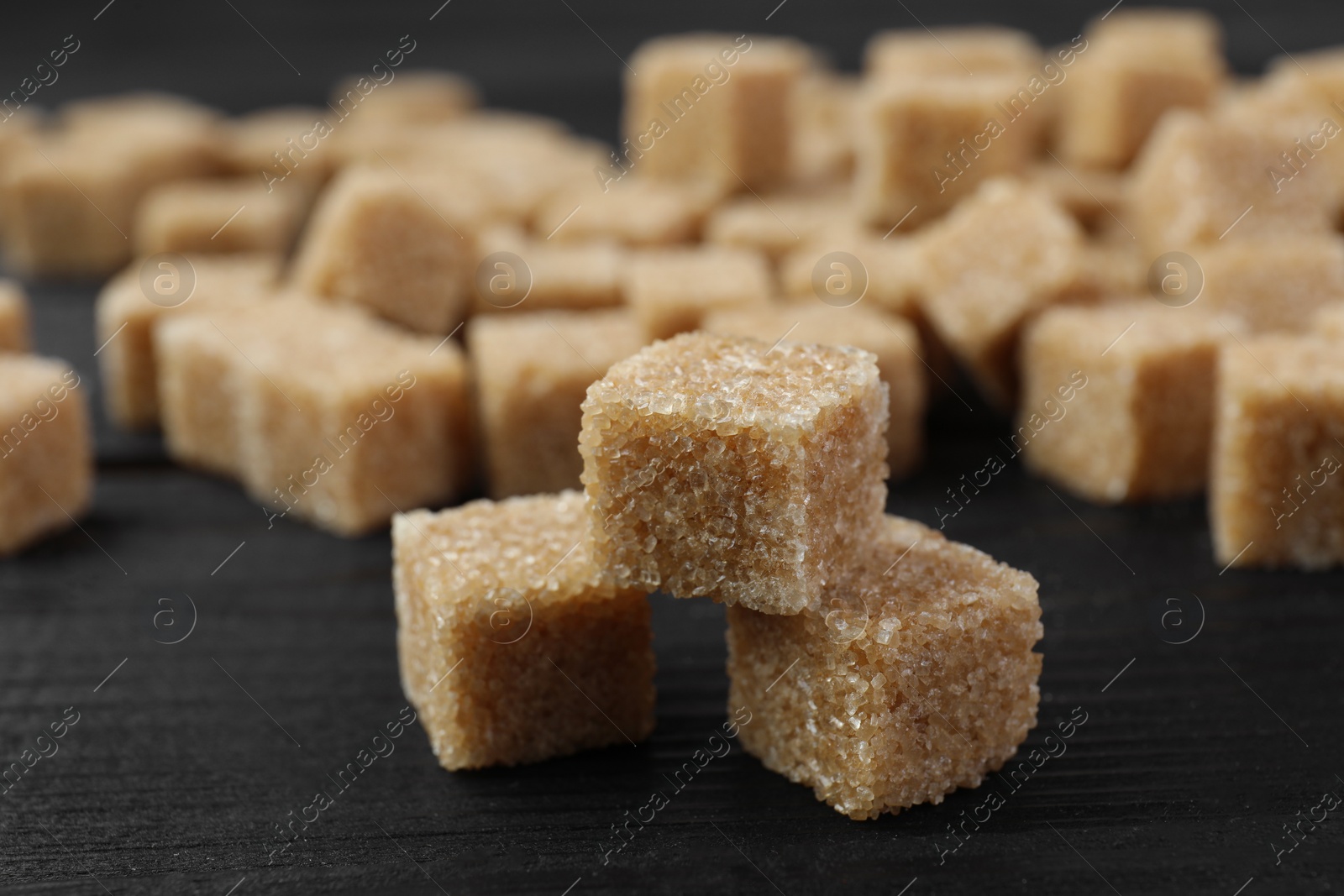 Photo of Brown sugar cubes on black wooden table, closeup