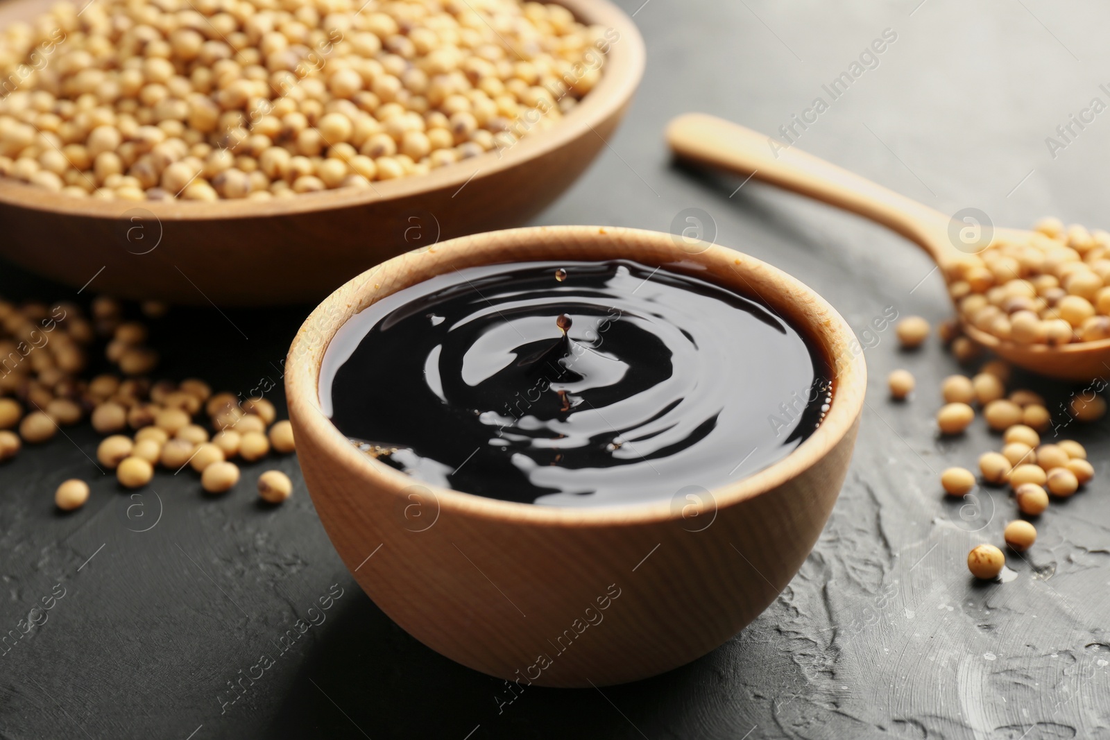 Photo of Tasty soy sauce in bowl and soybeans on black table, closeup