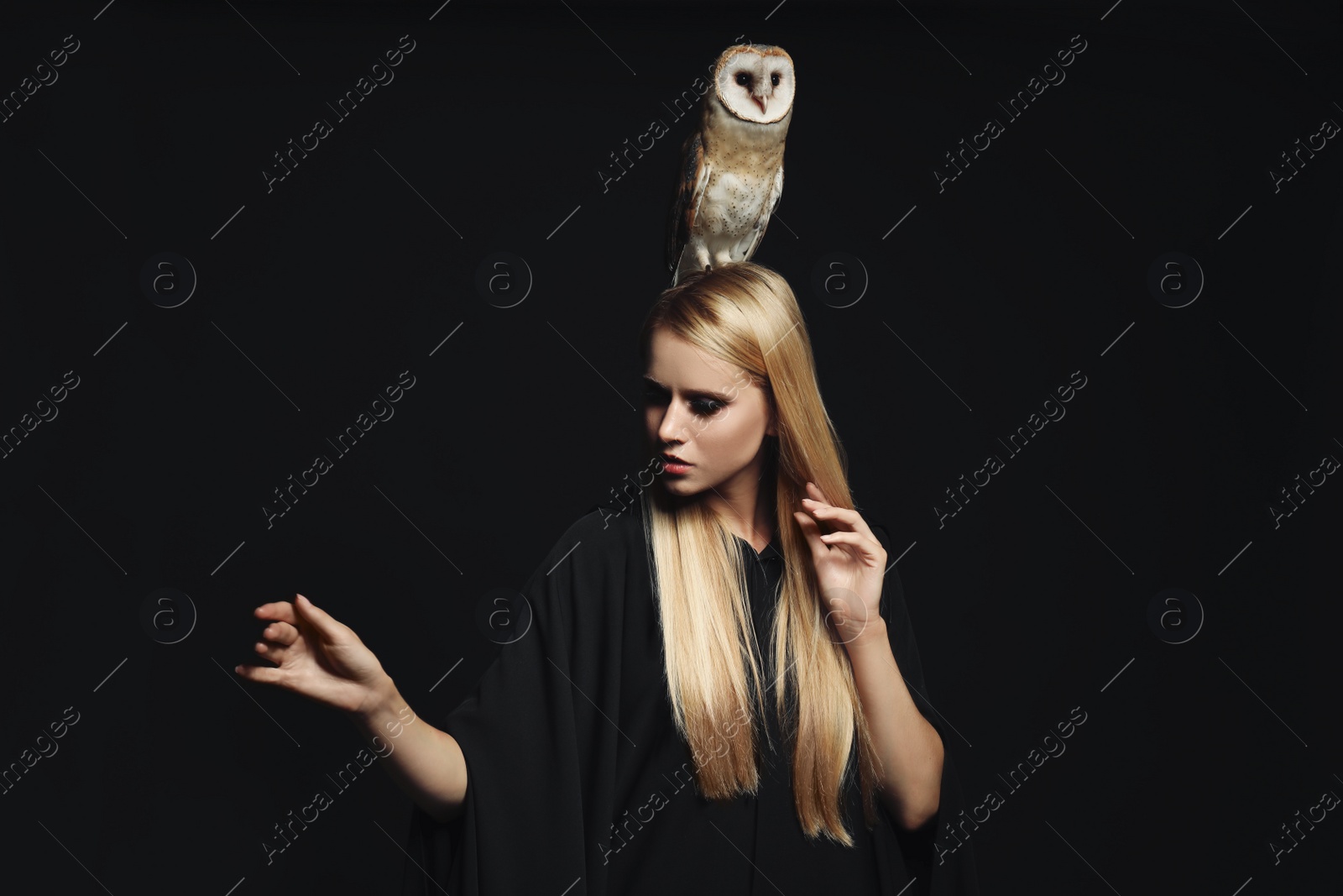 Photo of Witch in black mantle with owl on dark background. Scary fantasy character