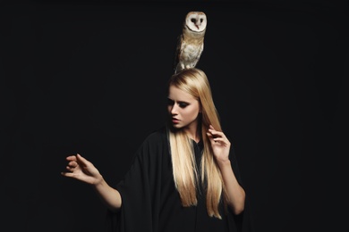 Photo of Witch in black mantle with owl on dark background. Scary fantasy character