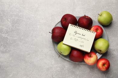 Photo of Notebook with calculated glycemic load for apples and fresh fruits on light grey textured table, top view. Space for text