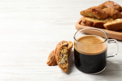 Photo of Tasty cantucci and cup of aromatic coffee on white wooden table, space for text. Traditional Italian almond biscuits