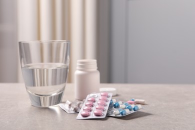Photo of Different pills in blisters, medical bottle and glass of water on grey table. Space for text