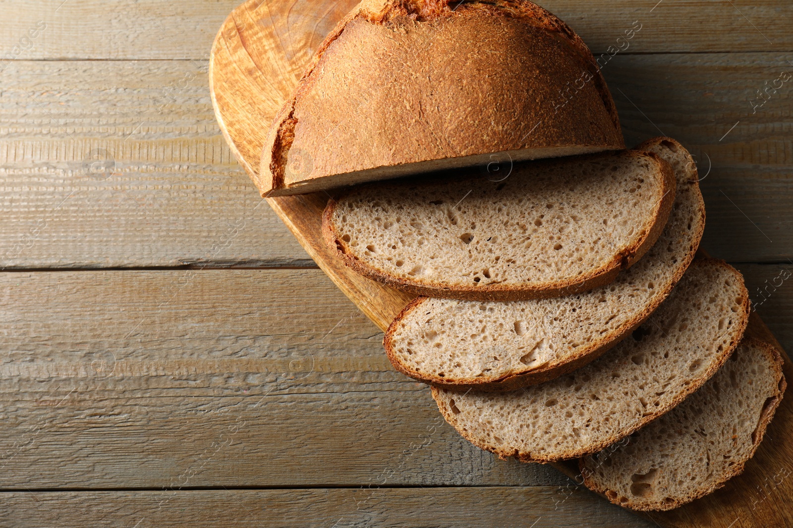 Photo of Freshly baked cut sourdough bread on wooden table, top view. Space for text