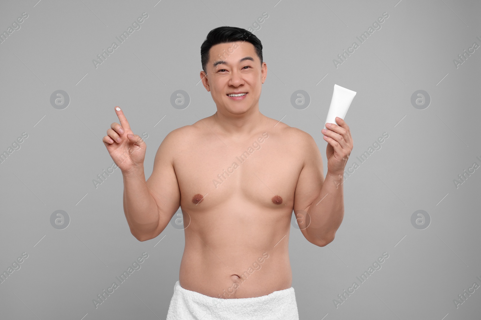 Photo of Handsome man with tube of body cream on light grey background