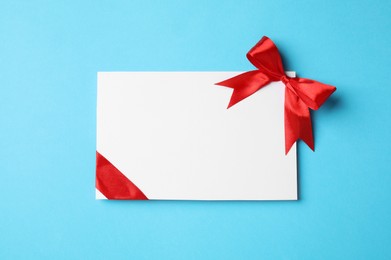 Photo of Blank gift card with red bow on light blue background, top view. Space for text