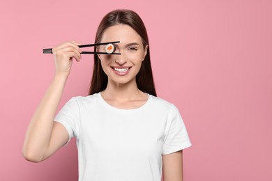 Funny young woman holding sushi roll with chopsticks on pink background. Space for text