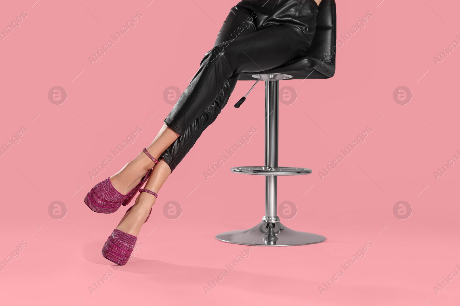 Photo of Woman wearing high heeled shoes with platform and square toes sitting against pink background, closeup