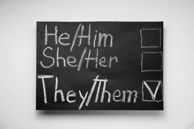 Photo of Gender equality. Small blackboard with written pronouns on beige background, top view