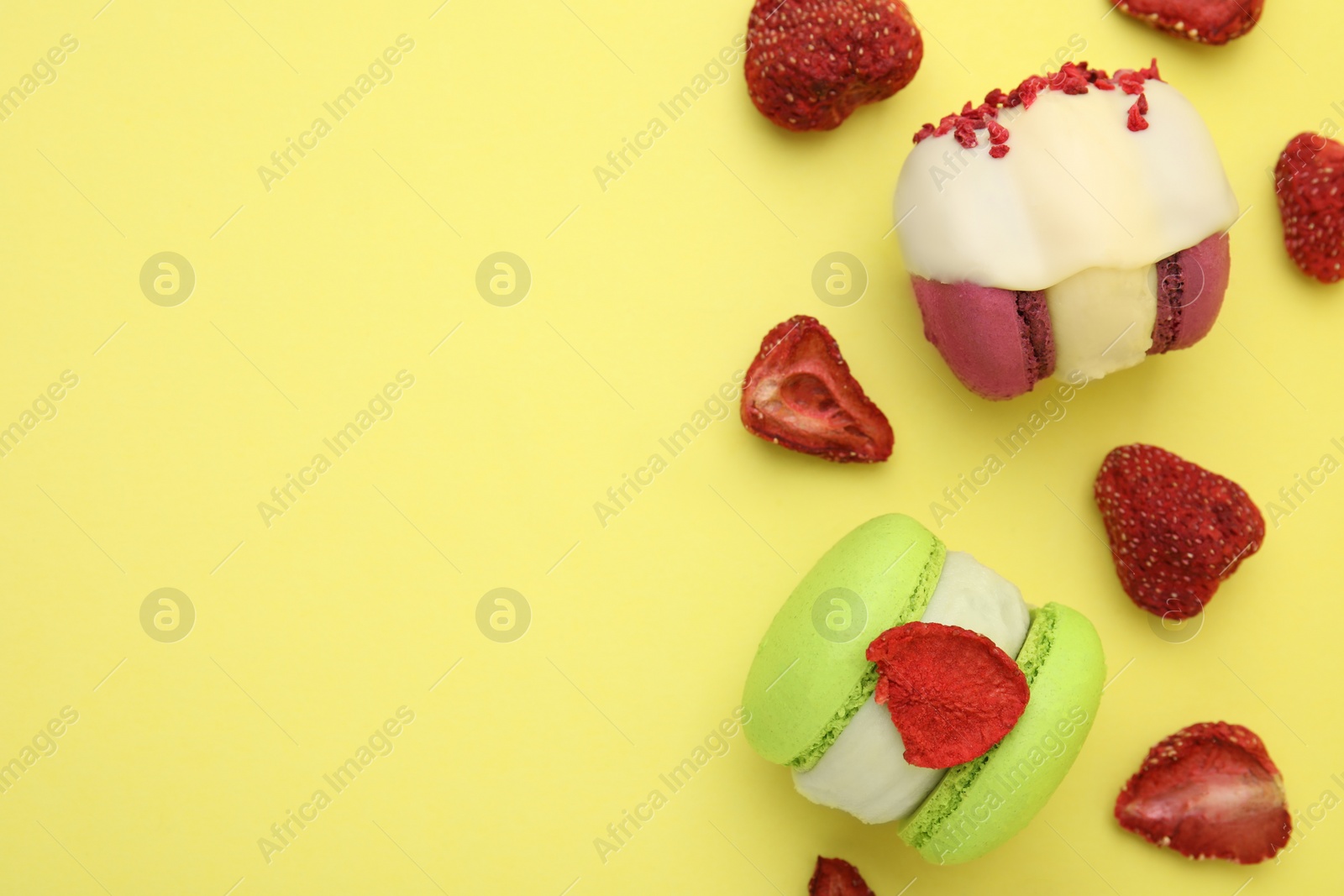 Photo of Delicious macarons and dry strawberries on yellow background, flat lay. Space for text