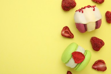 Delicious macarons and dry strawberries on yellow background, flat lay. Space for text