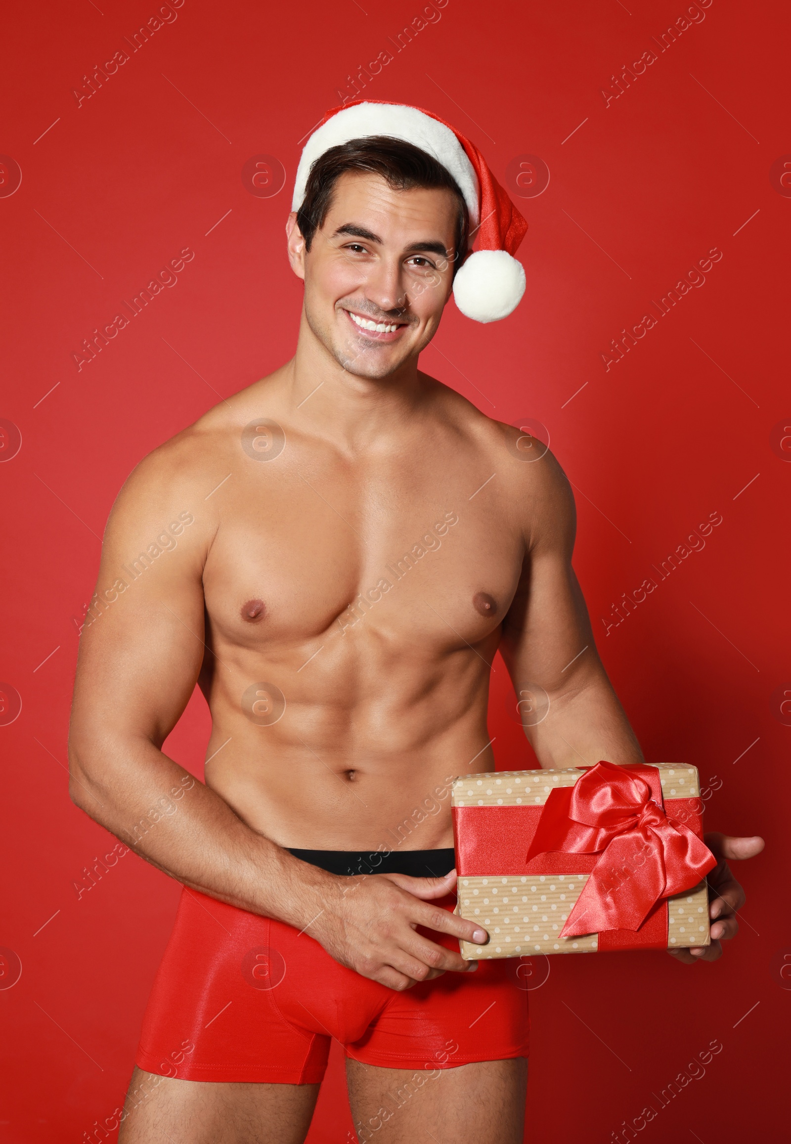 Photo of Sexy shirtless Santa Claus with gift on red background