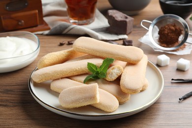 Photo of Tasty cookies with mint and other ingredients for tiramisu on wooden table, closeup
