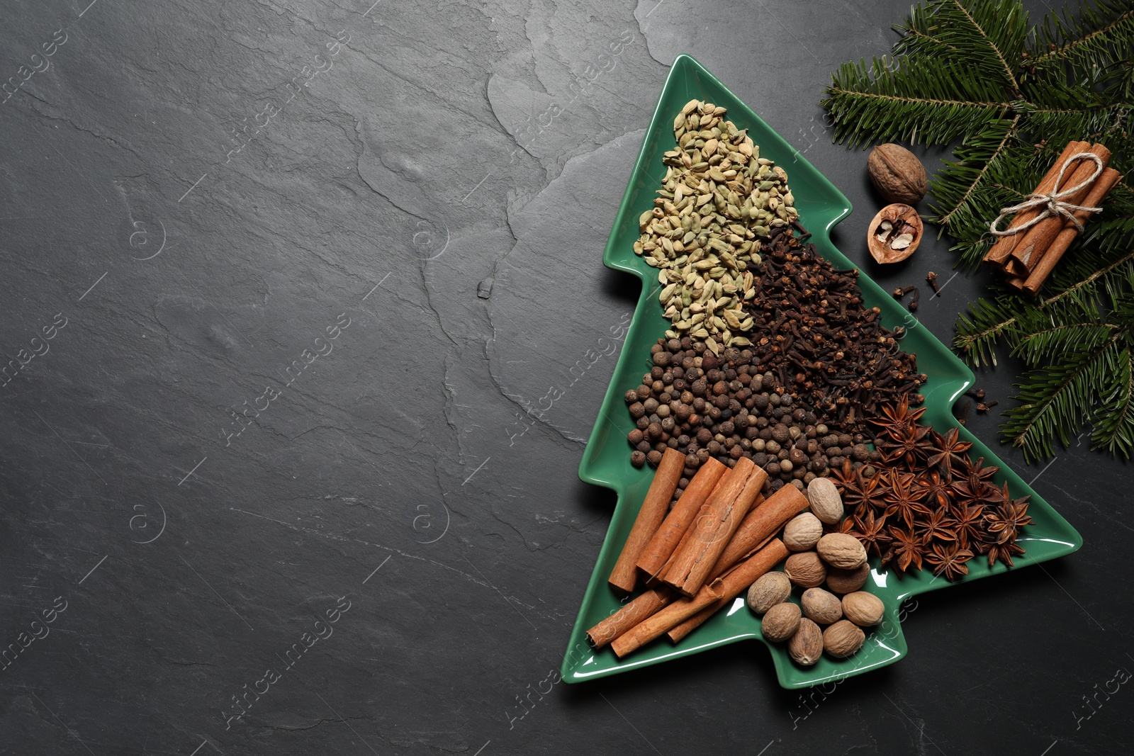 Photo of Different spices, nuts and fir branches on dark gray textured table, flat lay. Space for text