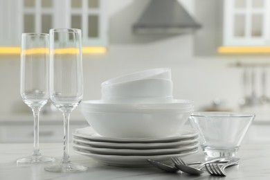 Photo of Different clean dishware, cutlery and glasses on white marble table in kitchen