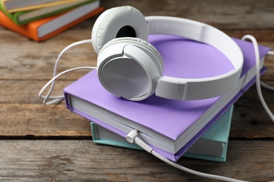 Photo of Modern headphones with hardcover books on wooden table
