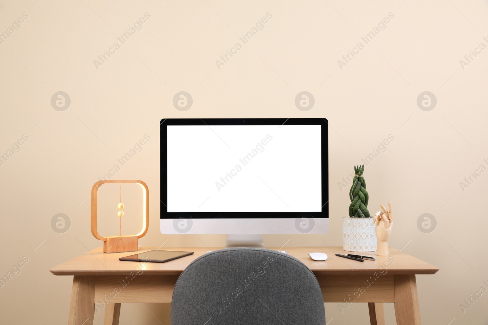 Photo of Comfortable workplace with blank computer display on desk and plant near beige wall. Space for text