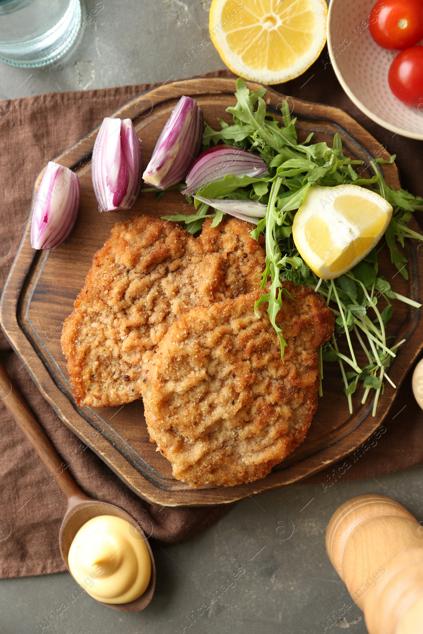 Photo of Delicious schnitzels served with lemon, onion and microgreens on grey table, flat lay