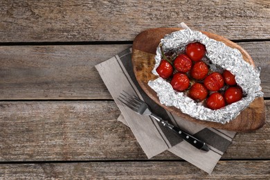 Photo of Aluminum foil with delicious baked tomatoes on wooden table, top view. Space for text