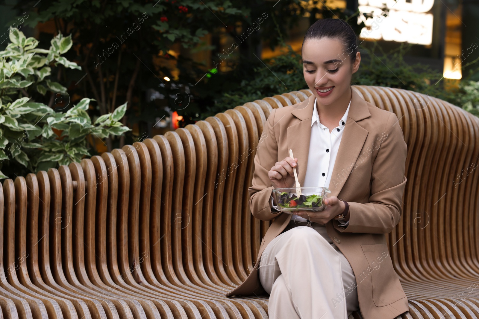 Photo of Happy young businesswoman eating lunch on bench outdoors