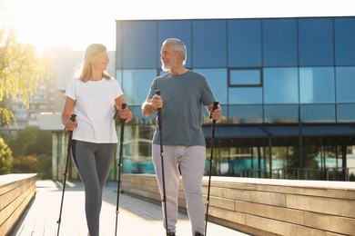 Happy senior couple practicing Nordic walking with poles outdoors on sunny day