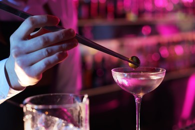 Photo of Bartender adding olive into Martini cocktail in bar, closeup