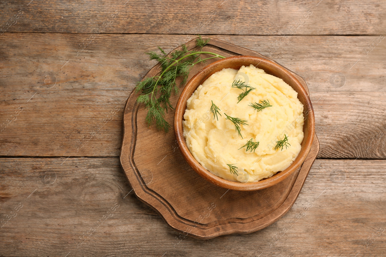 Photo of Bowl with mashed potatoes on wooden background, top view. Space for text