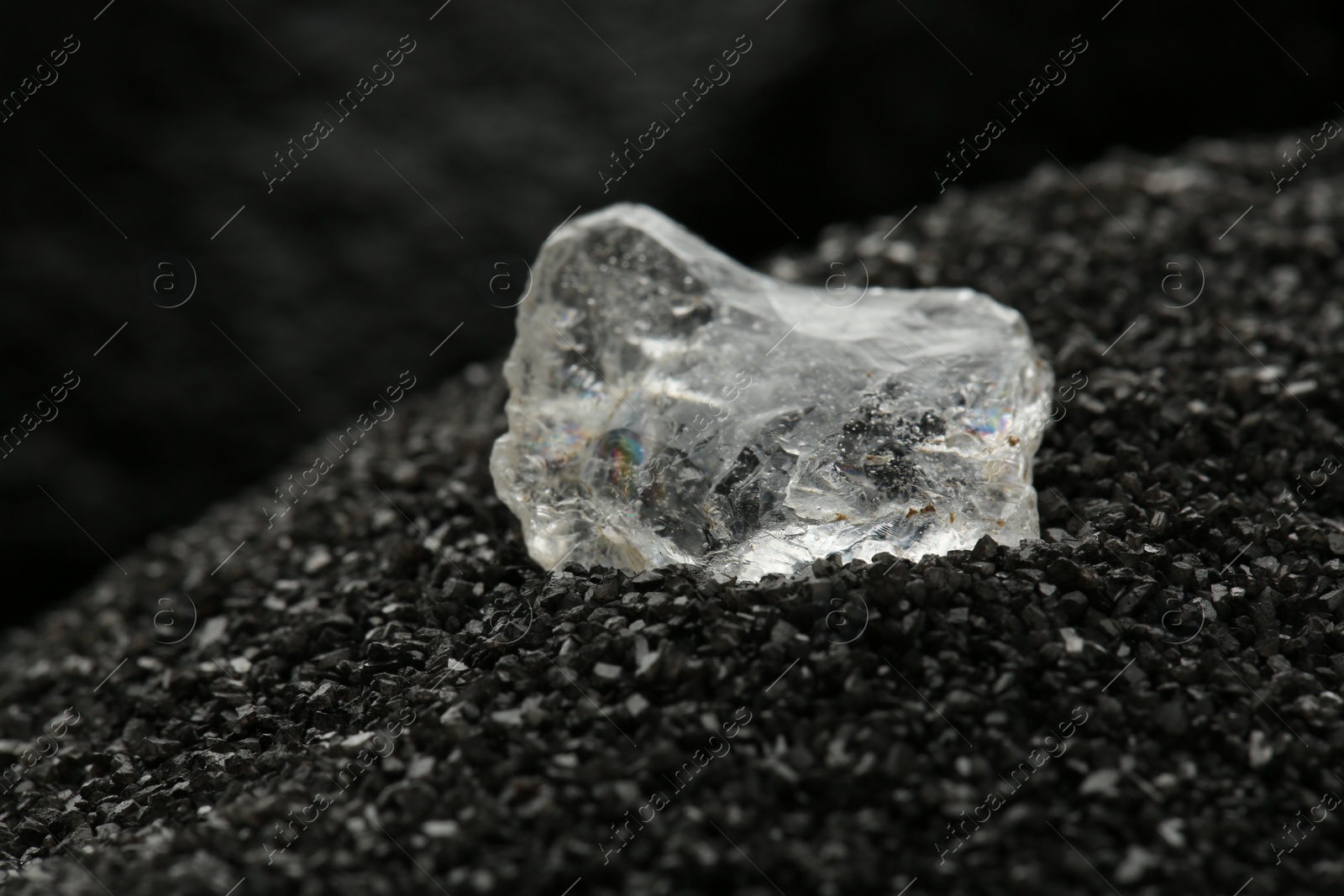 Photo of Shiny rough diamond on decorative black sand, closeup