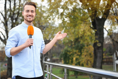 Young male journalist with microphone working in park. Space for text