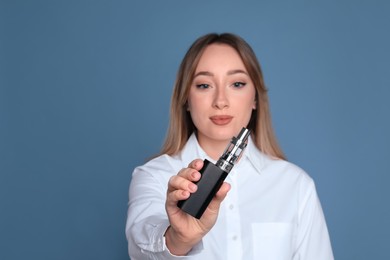 Young woman holding electronic cigarette against light blue background, focus on hand. Space for text