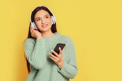 Young woman listening to audiobook on yellow background