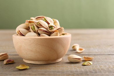 Tasty pistachios in bowl on wooden table against olive background, closeup. Space for text