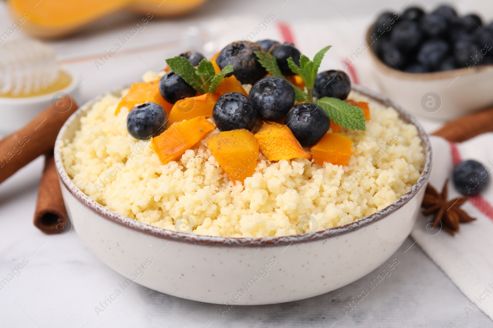 Photo of Bowl of tasty couscous with blueberries, pumpkin and mint on table, closeup
