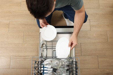 Photo of Man loading dishwasher with glasses and plates, top view