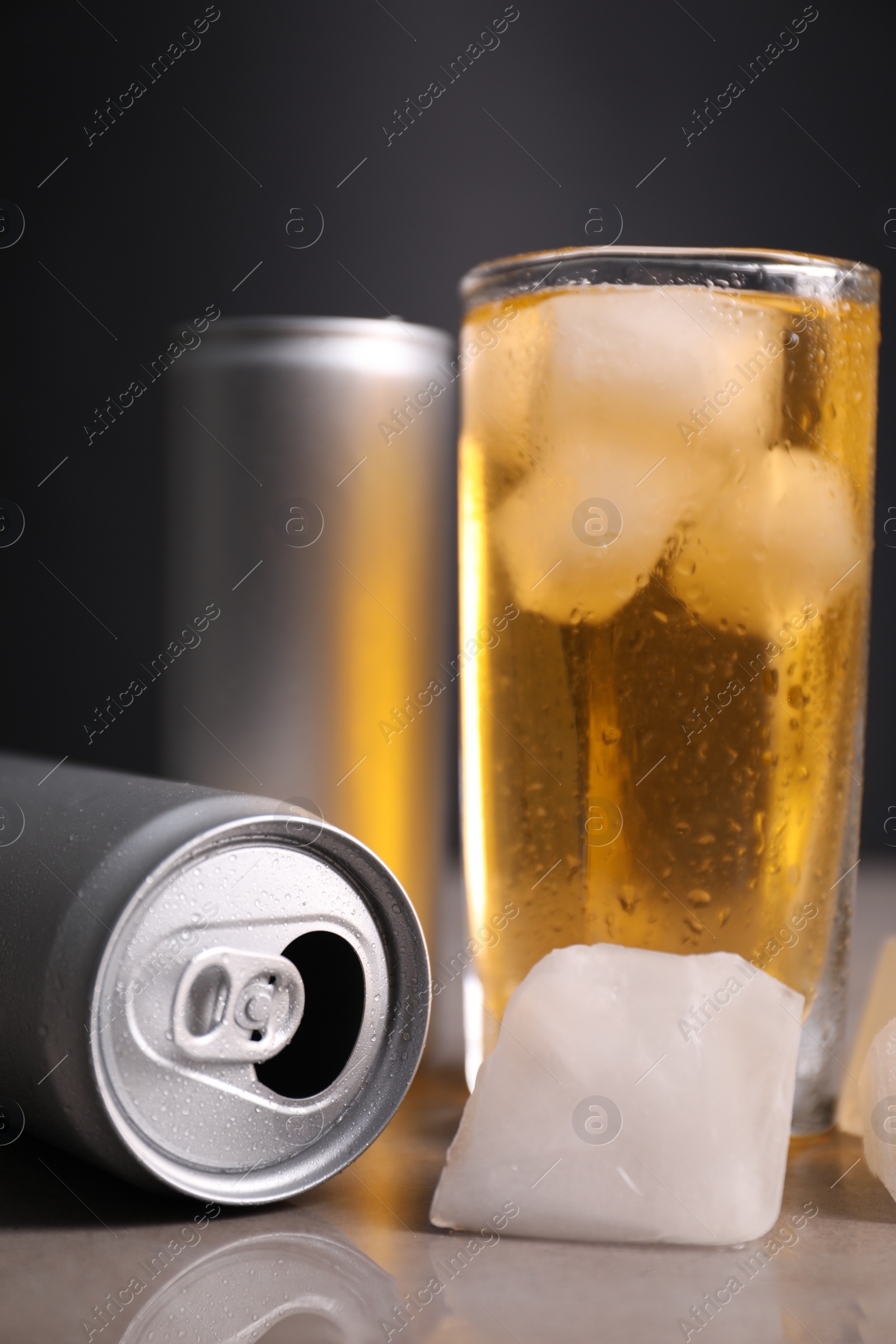 Photo of Tasty energy drink with ice cubes in glass and aluminium cans on grey table, closeup