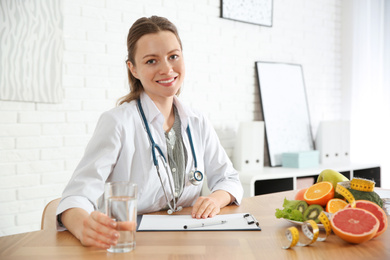 Photo of Nutritionist with glass of water and clipboard at desk in office