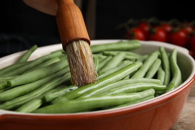 Photo of Woman brushing raw green beans with oil, closeup